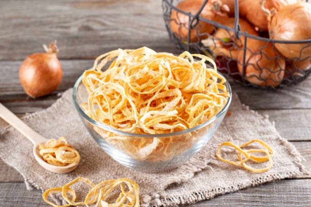 Dried onion rings in a glass bowl on a wooden table. Spices and food ingredients
