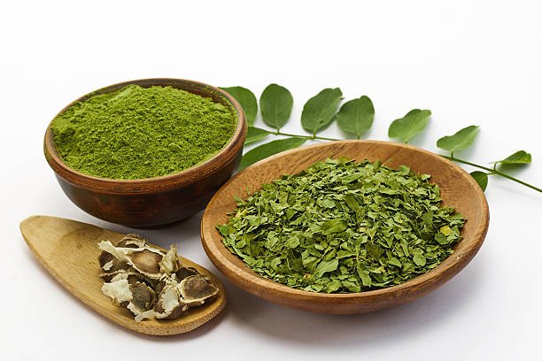 Top view of moringa powder, leaves, oil, and seeds on a white background.